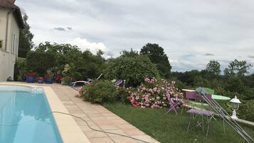 Ein Schwimmbecken mit gefliestem Rand, umgeben von Kübelpflanzen und einer Rasenfläche mit Gartenmöbeln.