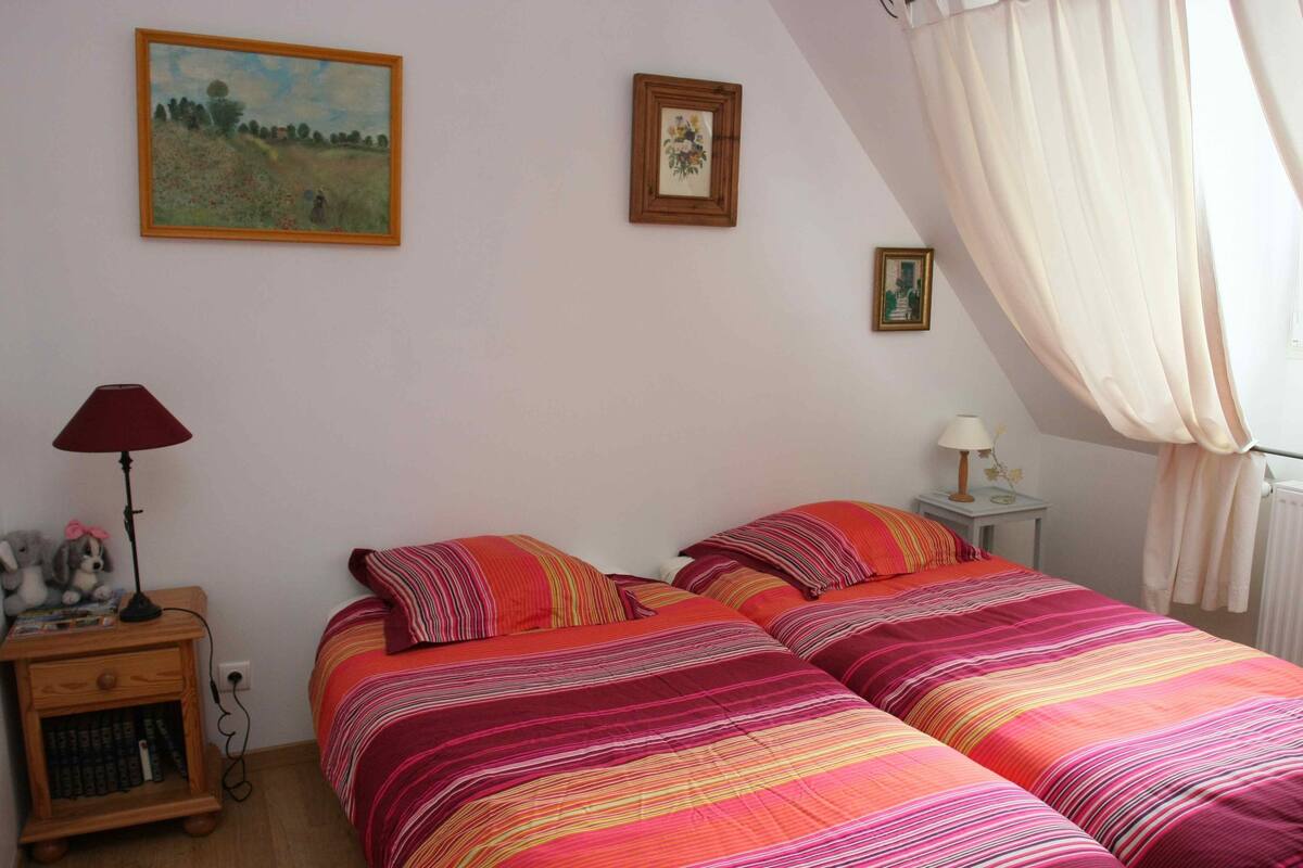 A bedroom with two beds, a nightstand, a lamp, and two framed pictures on the wall.