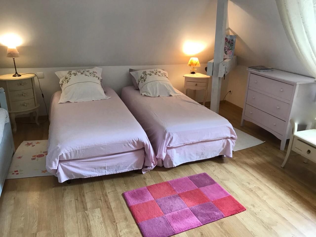 Un dormitorio con dos camas, mesitas de noche con lámparas, un aparador y una alfombra rosa y morada.