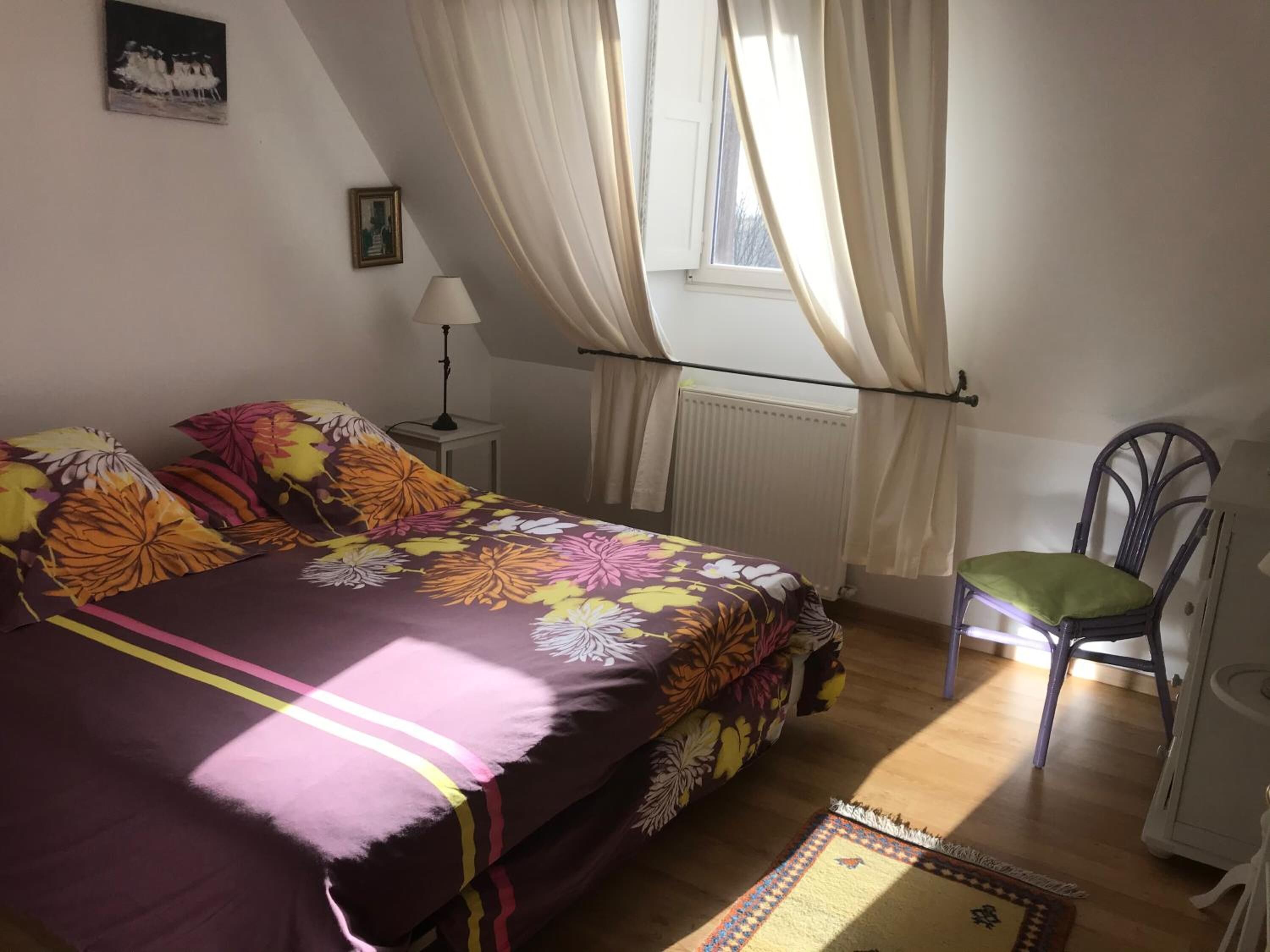 Ein Schlafzimmer mit Bett, Stuhl, Lampe und Vorhängen.