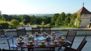 A round table set for a meal with chairs around it, overlooking a scenic landscape with trees and a distant view of hills. - La Maison Du Parc (Saint-Raphaël)