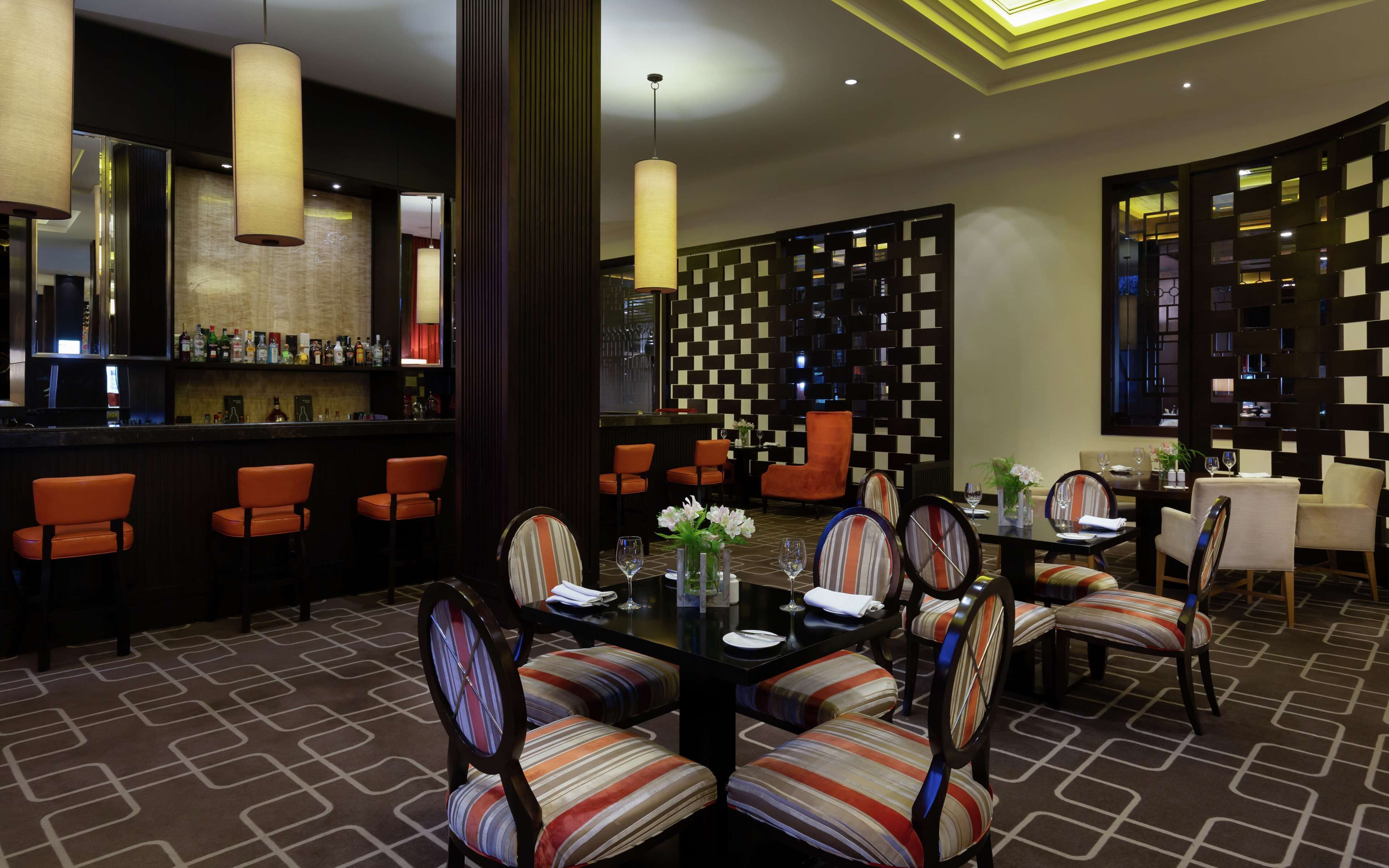 A modern dining area with striped chairs, a bar with bottles, and a patterned wall.