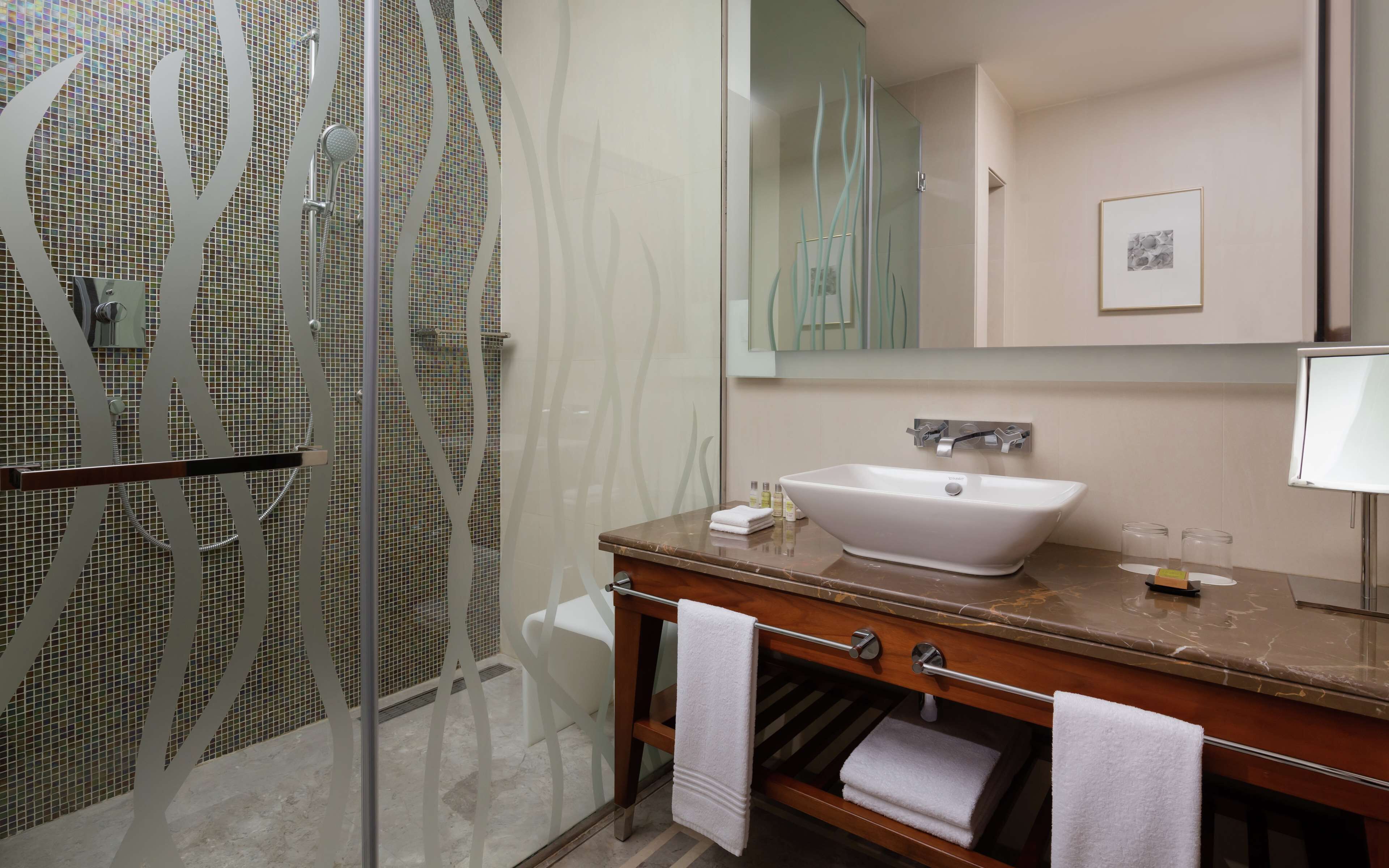 Un baño con cabina de ducha de cristal, un lavabo blanco y un mueble de tocador de madera.