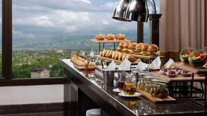 Un tavolo del buffet con diversi cibi e vista sulla città attraverso una finestra.