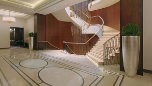 Una hall d'albergo moderna con una scala a chiocciola, una pianta in vaso di grandi dimensioni e un pavimento in marmo lucidato.