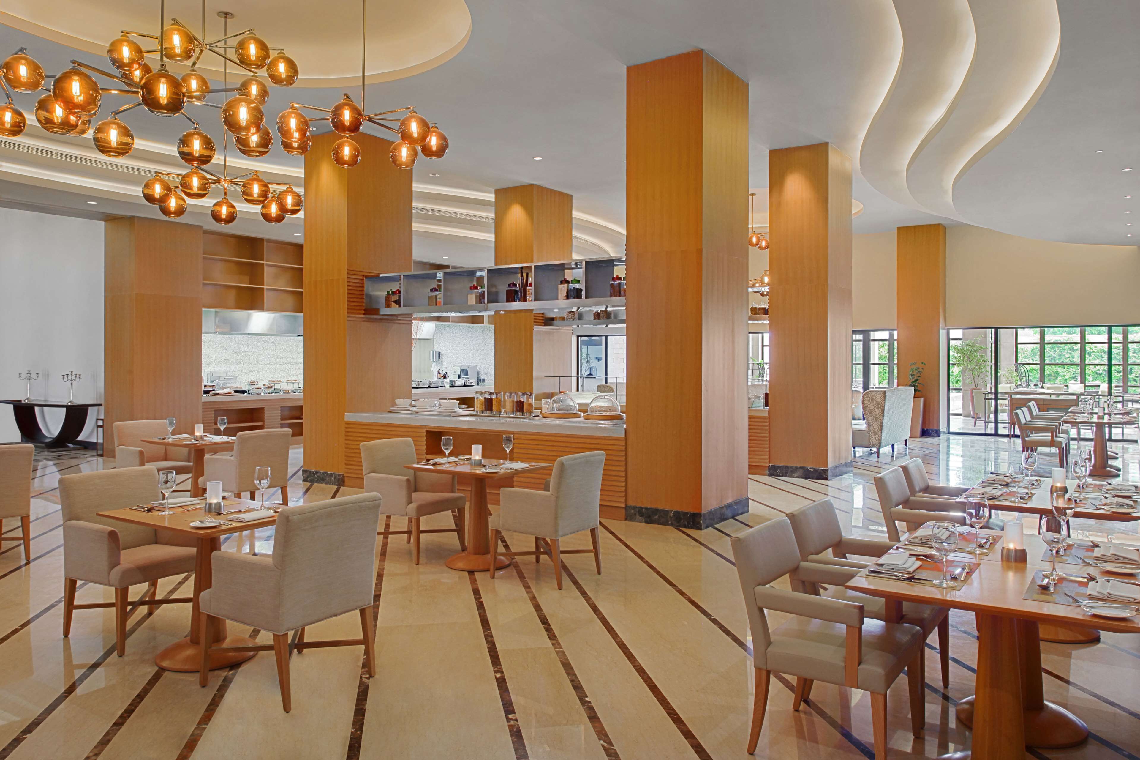 Un espace de restauration moderne avec plusieurs tables et chaises, un bar central et une cuisine en arrière-plan.