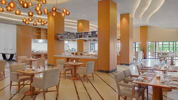 Un espace de restauration moderne avec plusieurs tables et chaises, un bar central et une cuisine en arrière-plan.