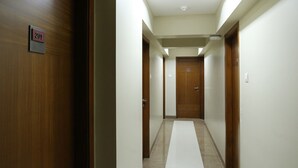 A hotel corridor with wooden doors, a white tiled floor, and a skylight. - Hotel Bombay International (Mumbai)