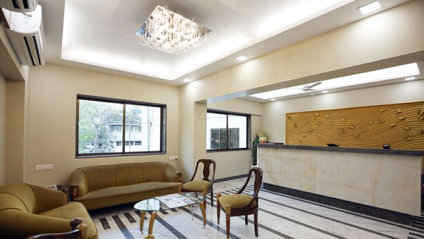 A modern reception area with a sofa, chairs, a reception desk, and large windows. - Hotel Bombay International (Mumbai)