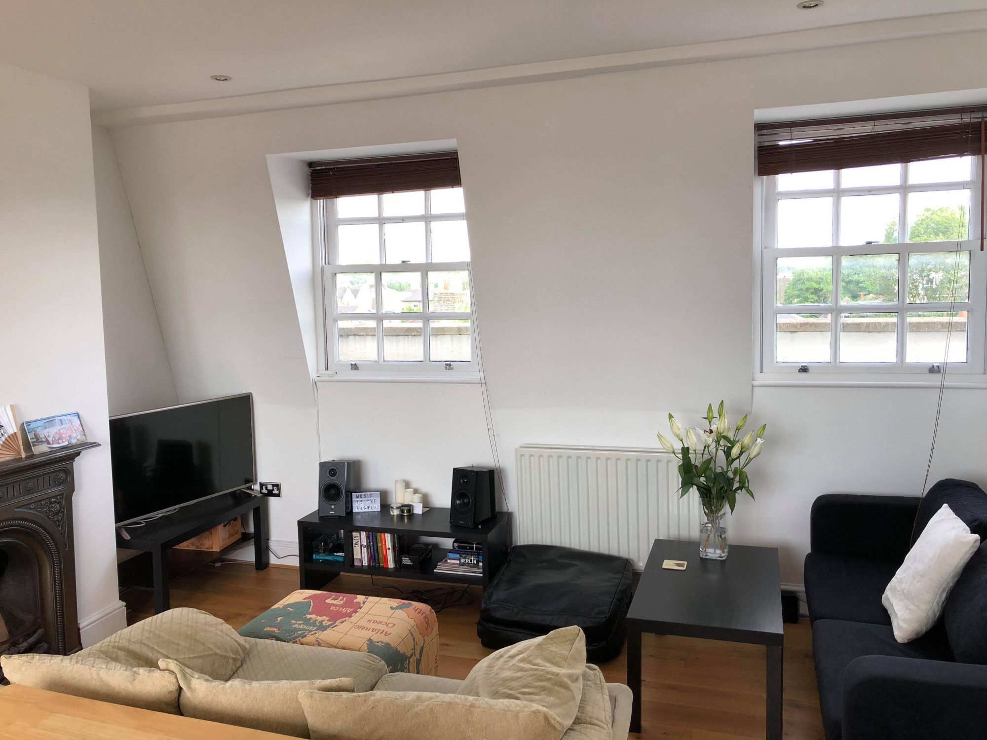 Een woonkamer met een televisie, zwarte banken, een salontafel en een boekenkast.