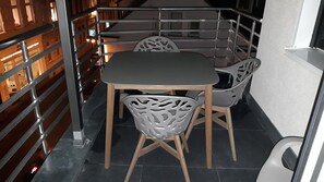 Pequeña zona de balcón cerrada con una mesa y sillas, barandillas de metal y vistas a la calle.