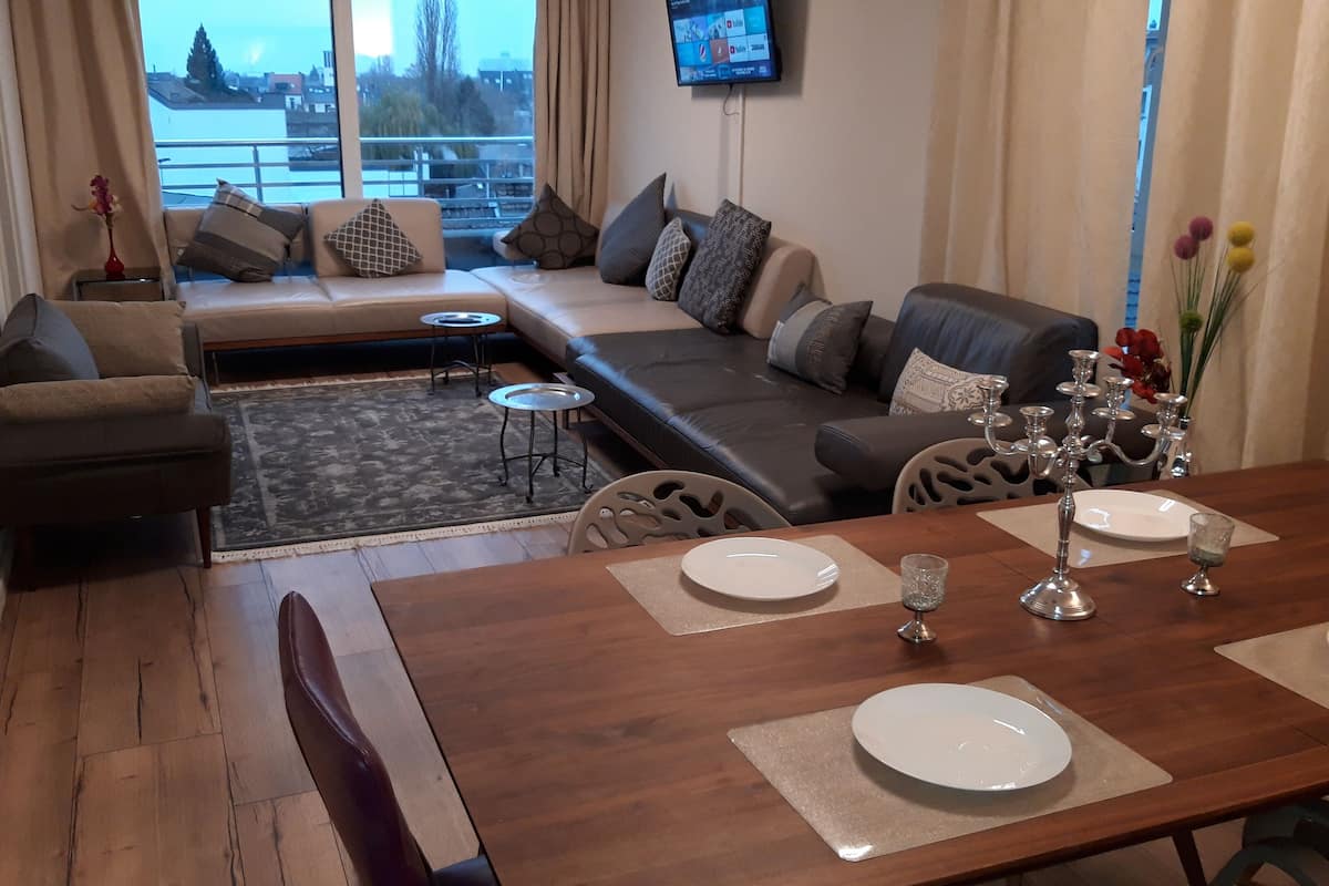 A modern living room with a sofa set, a dining table set for four, and a view of the city through large windows.