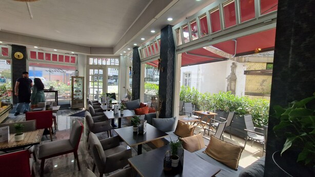 Un café con mesas dentro, ventanas amplias y vistas a la calle.