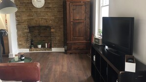 A living room with a brick fireplace, a wooden cabinet, a television, and a lamp. - The Portobello Loft (London)
