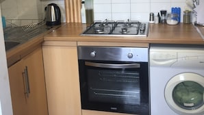 A compact kitchen with wooden cabinets, a gas stove, a dishwasher, and a built-in oven. - The Portobello Loft (London)