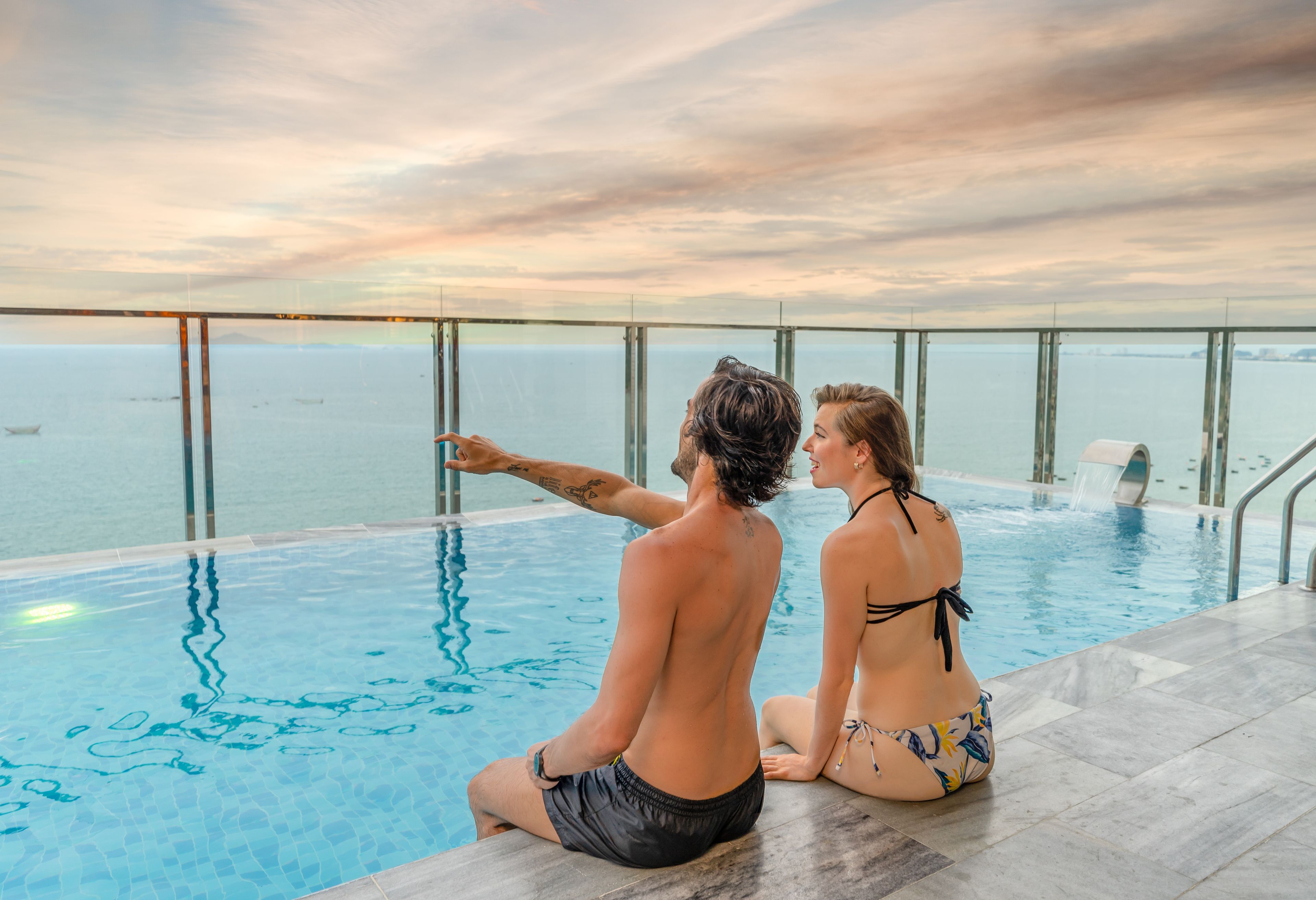 Una pareja sentada junto a una piscina infinita con vistas al mar.
