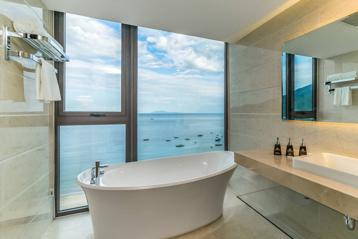 Ein modernes Badezimmer mit freitragender Badewanne, einem großen Spiegel und Meerblick.