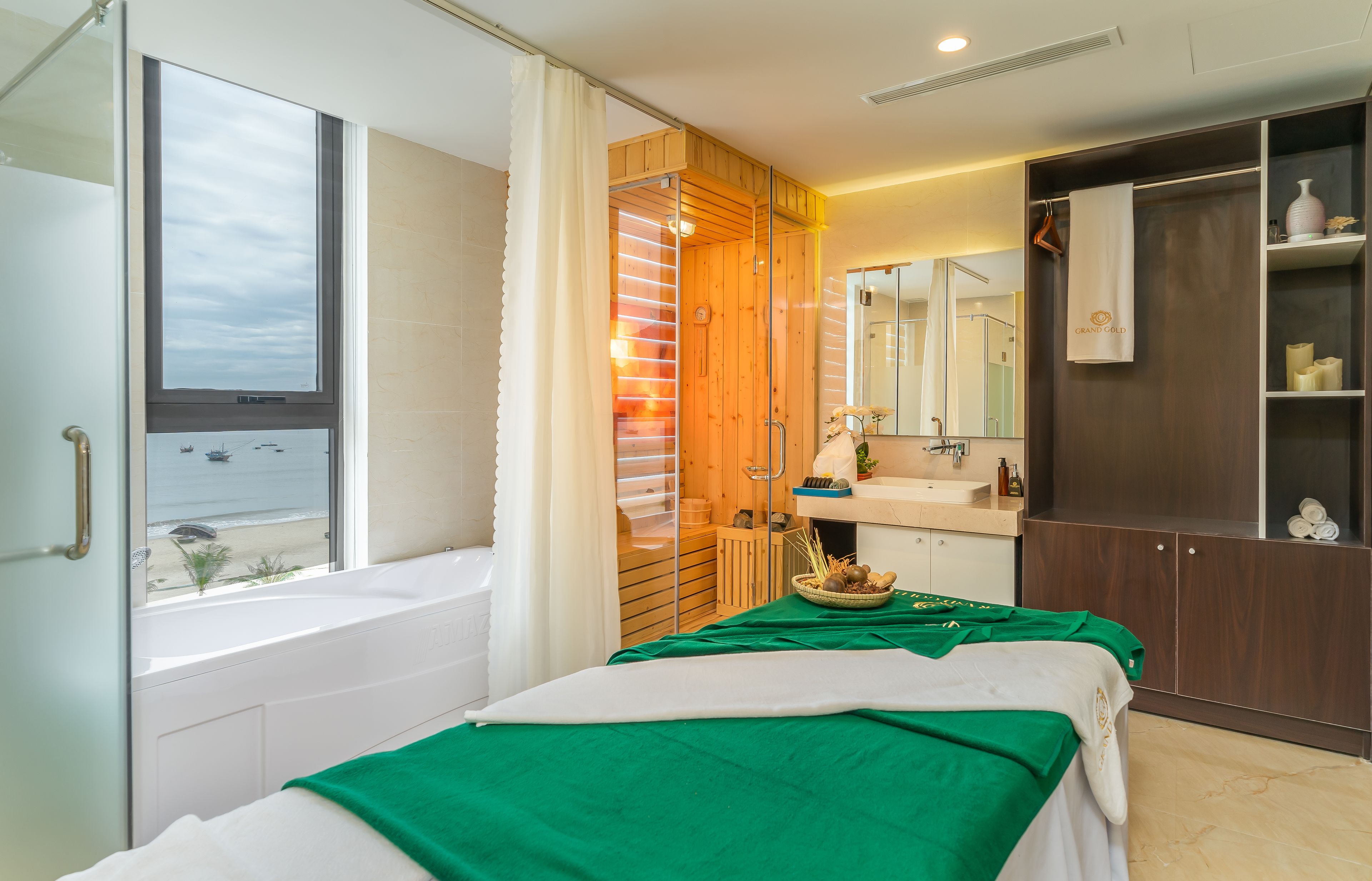 A modern hotel room with a large window, a bathtub, a wooden sauna, a green bedspread, and a vanity with a mirror.