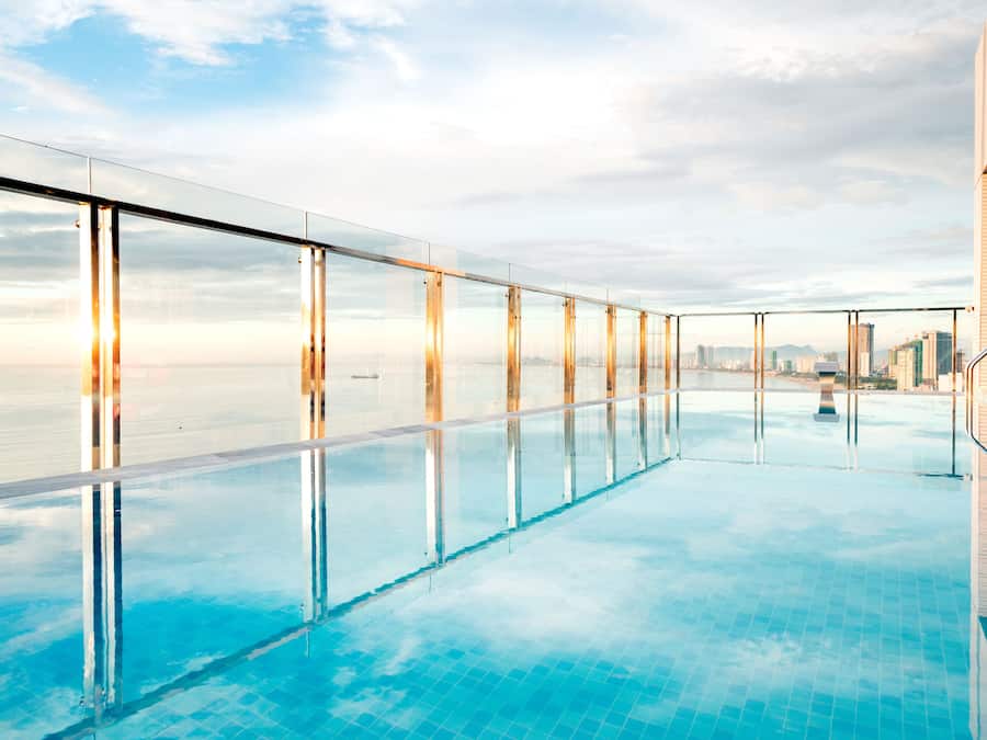 Une piscine à débordement située sur le toit, dotée de garde-corps en verre transparent et offrant une vue sur la ville.