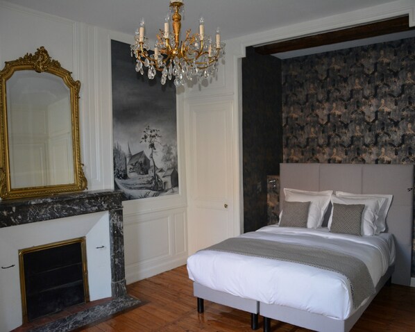 Une chambre à coucher avec un lit, un lustre, une cheminée, un grand miroir et un mur orné de motifs.