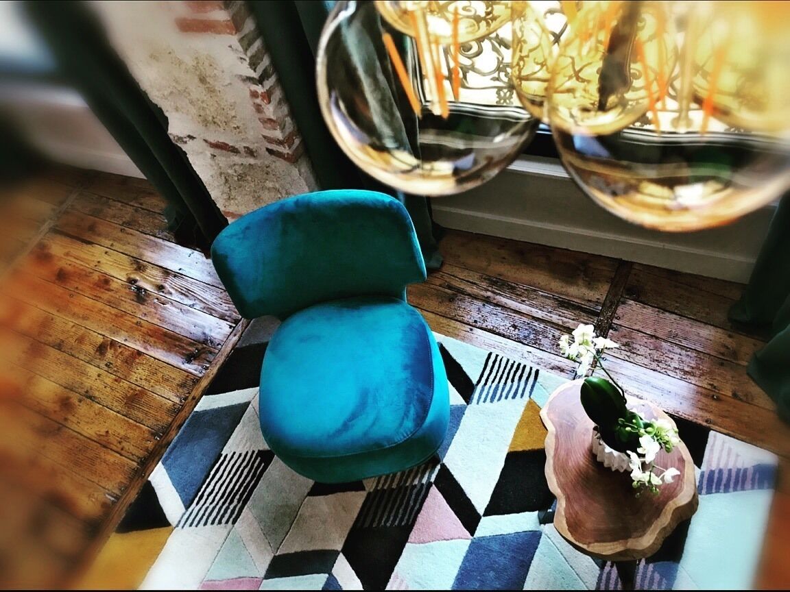 A room with a blue chair, a patterned rug, and a small table with a plant.