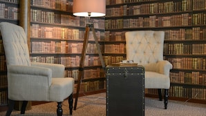 Une salle de bibliothèque avec deux fauteuils, une lampe sur pied et un coffre.