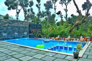 A swimming pool with a stone wall, lounge chairs, and potted plants. - Tree Blanche Munnar (Devikolam)
