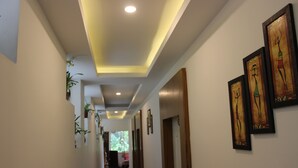 A hallway with recessed lighting, framed artwork on the walls, and potted plants. - Tree Blanche Munnar (Devikolam)