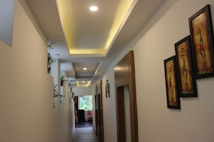 A hallway with recessed lighting, framed artwork on the walls, and potted plants.