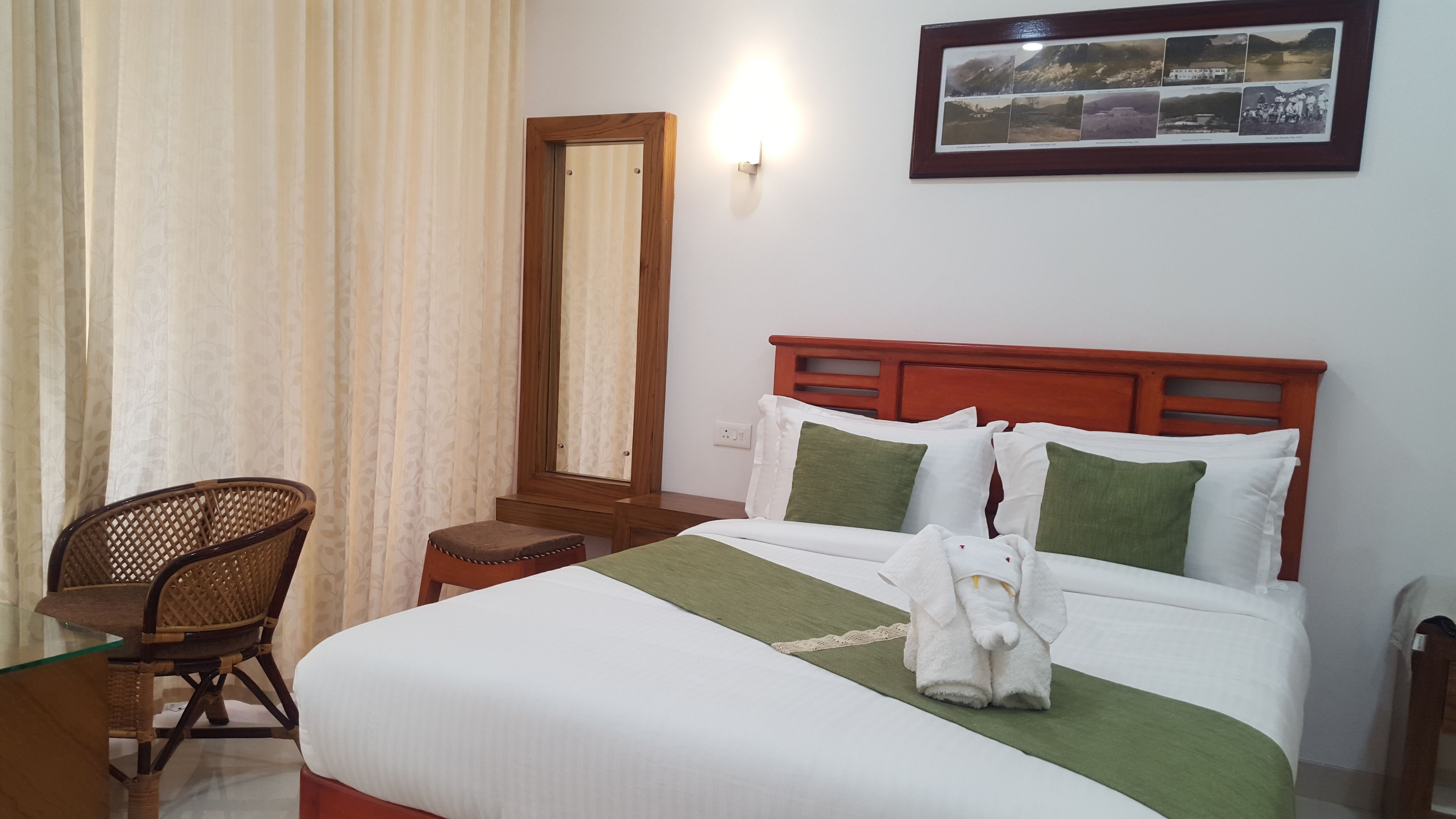 Una habitación de hotel con cama, una silla, mesita de noche, espejo y una foto enmarcada en la pared.