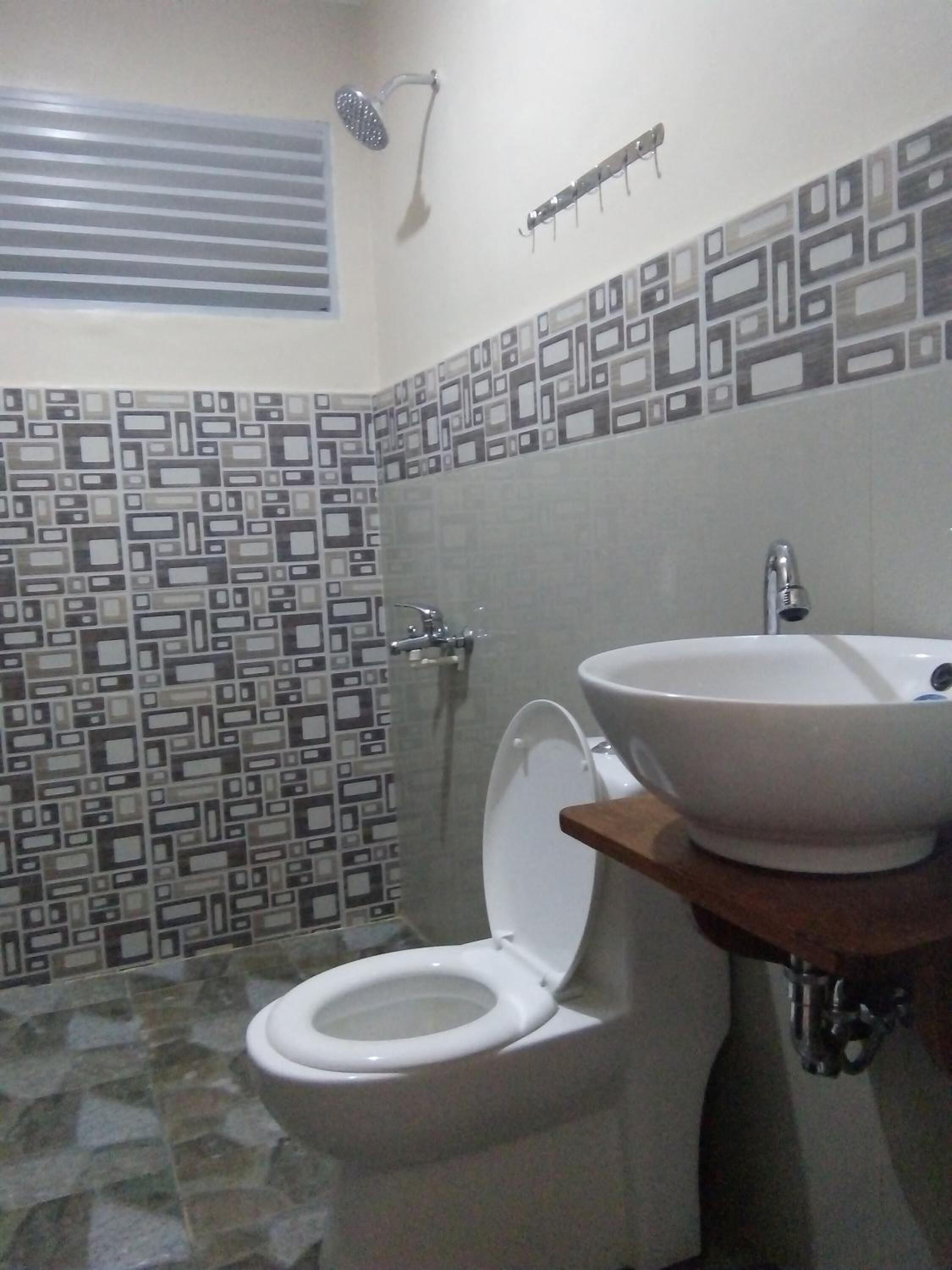 A bathroom with a toilet, a sink, a shower, and a patterned wall.