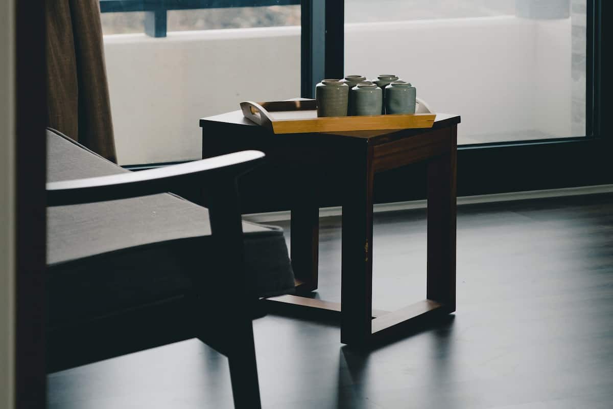 Una habitación con un gran ventanal, una mesa de madera con recipientes de cerámica y una silla.