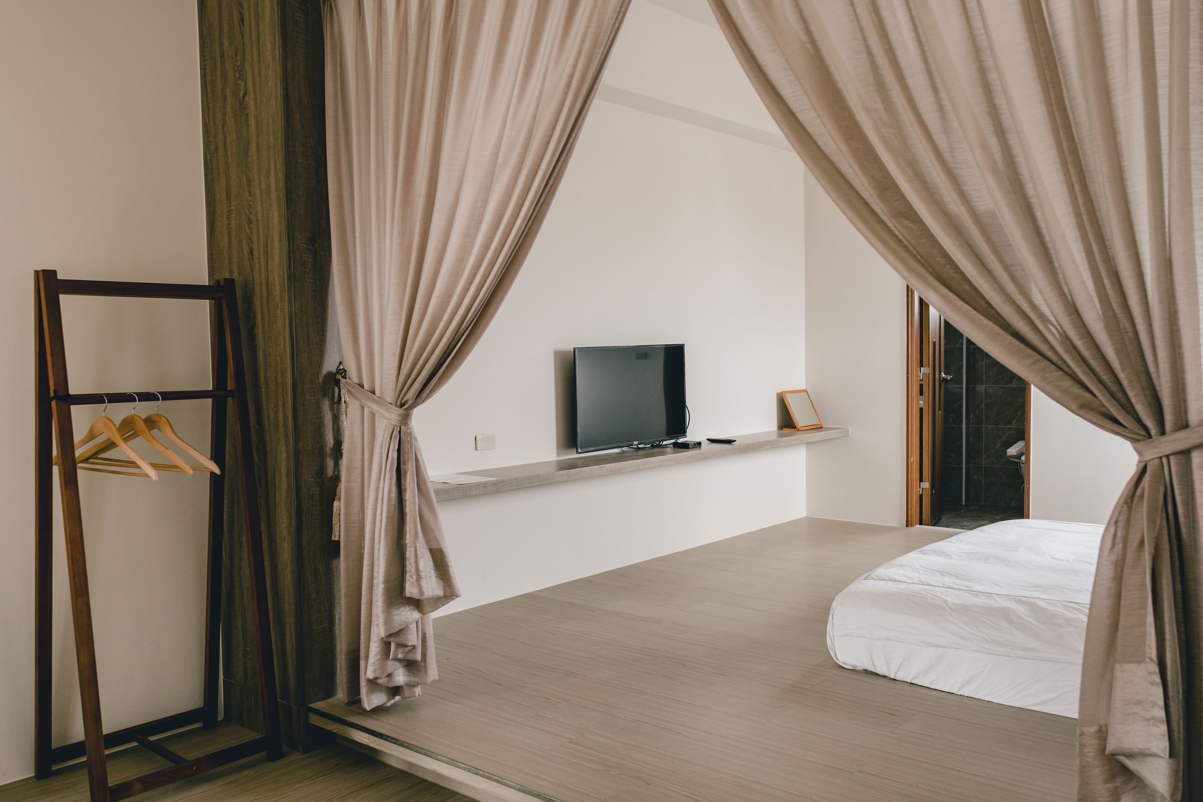 Un dormitorio con cama, televisor en una estantería y un perchero de madera.
