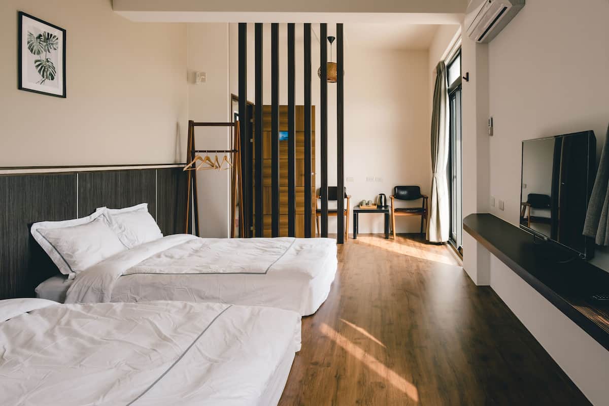 Habitación de hotel con dos camas, suelo de madera, televisión y un amplio ventanal con cortinas.
