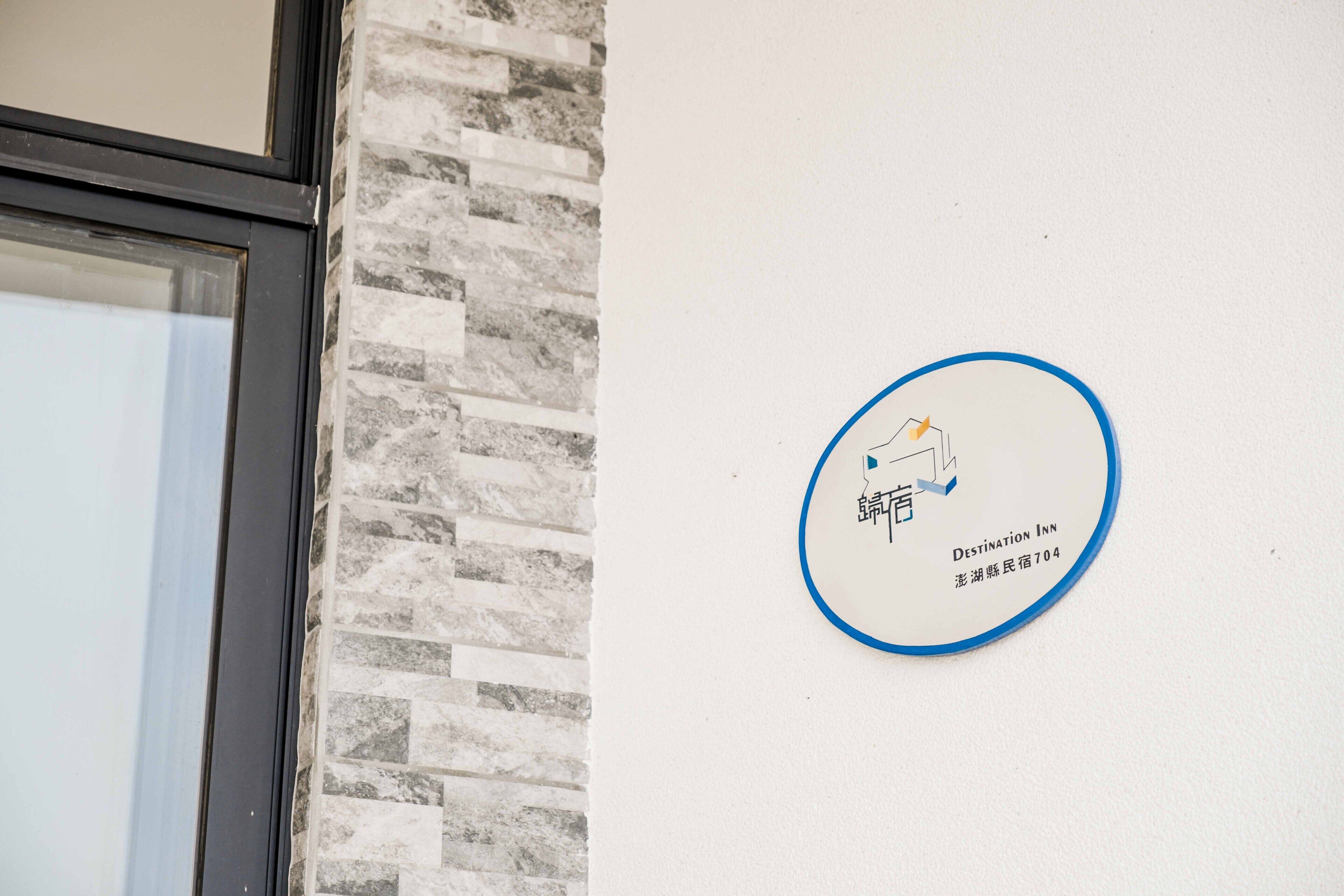 Schild des Destination Inn mit Logo und Adresse an einer weißen Wand.