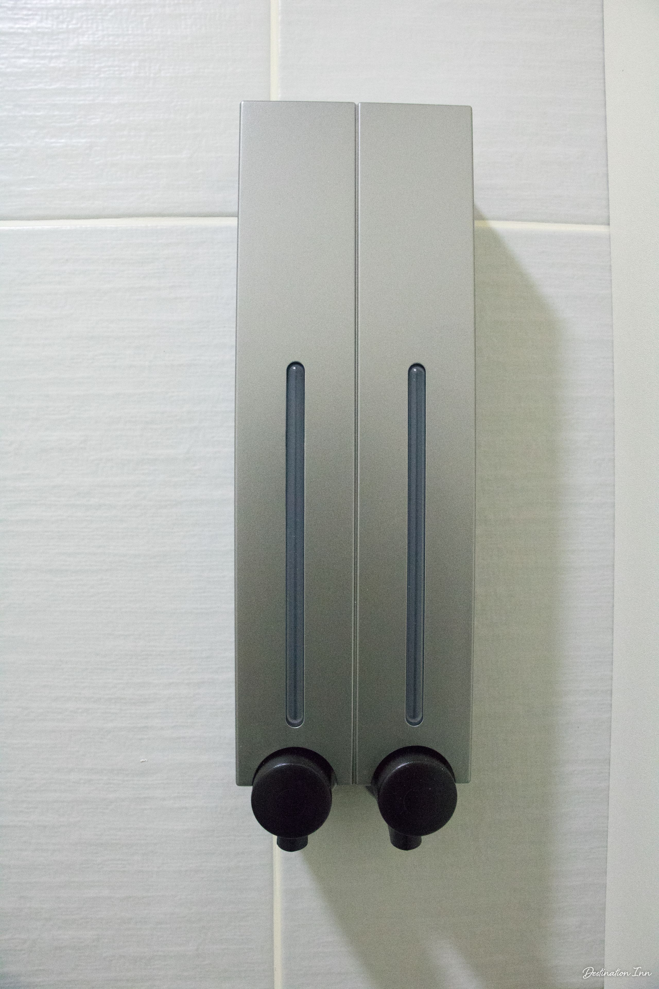 Een metalen, rechthoekig object met twee verticale handgrepen en twee ronde knoppen, bevestigd aan een witte betegelde muur.
