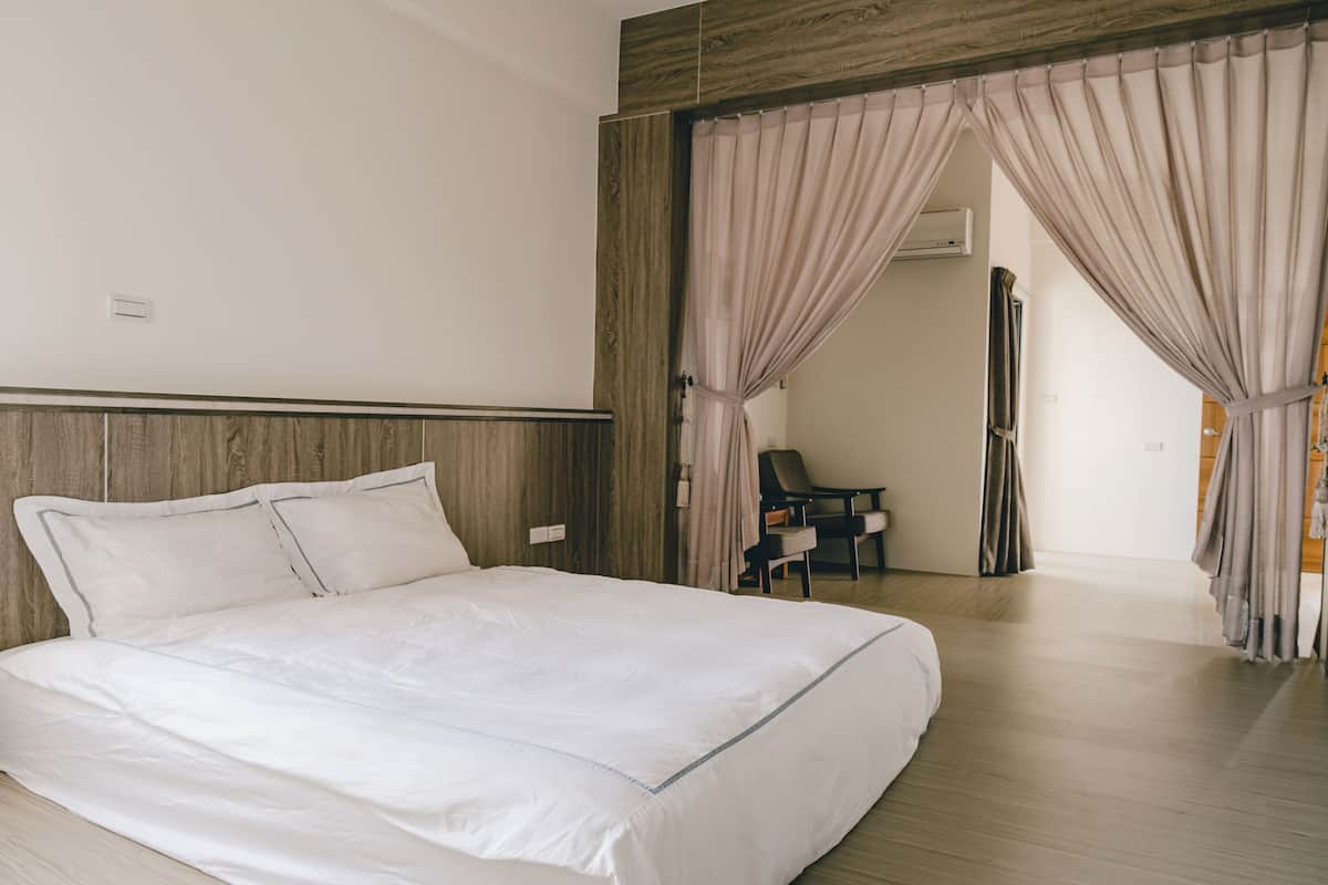 Un dormitorio moderno con una cama grande, cabecera de madera y vista a un pasillo con una silla y cortinas.