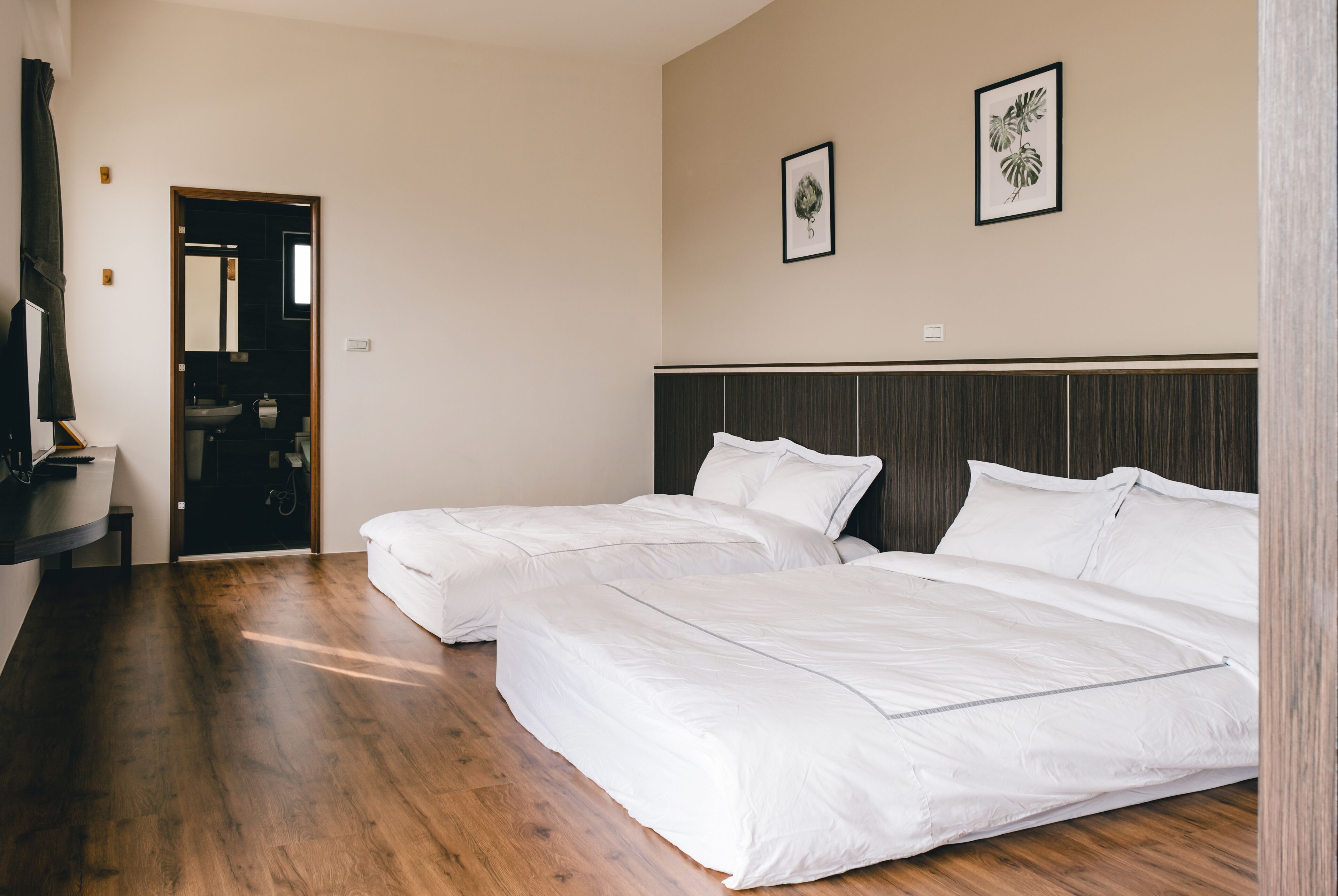 A hotel room with two beds, a wooden floor, a dark headboard, and a mirror on the wall.