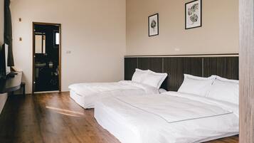 A hotel room with two beds, a wooden floor, a dark headboard, and a mirror on the wall.