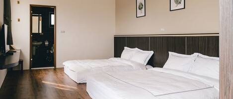 A hotel room with two beds, a wooden floor, a dark headboard, and a mirror on the wall.