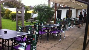 An outdoor patio with tables and chairs, a covered area, and a person in the background. - The White Hart Inn (Twickenham)