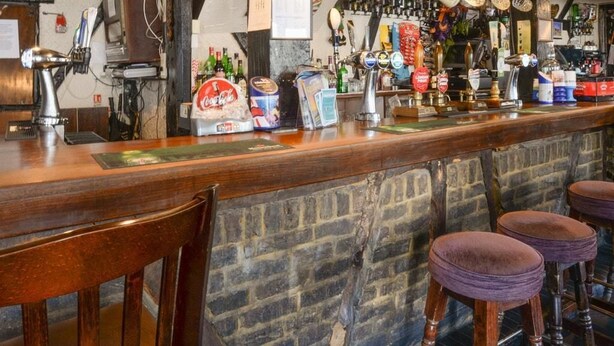 A bar with a wooden counter, stools, and a brick wall. - The White Hart Inn (Twickenham)