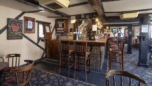 A bar with wooden chairs and a bar counter, featuring a rustic interior with exposed beams and a patterned carpet. - The White Hart Inn (Twickenham)