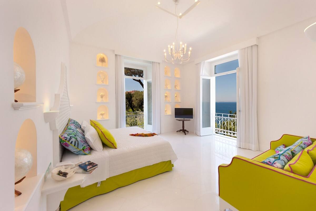 A bright bedroom with a bed, a TV, and a balcony with a view.