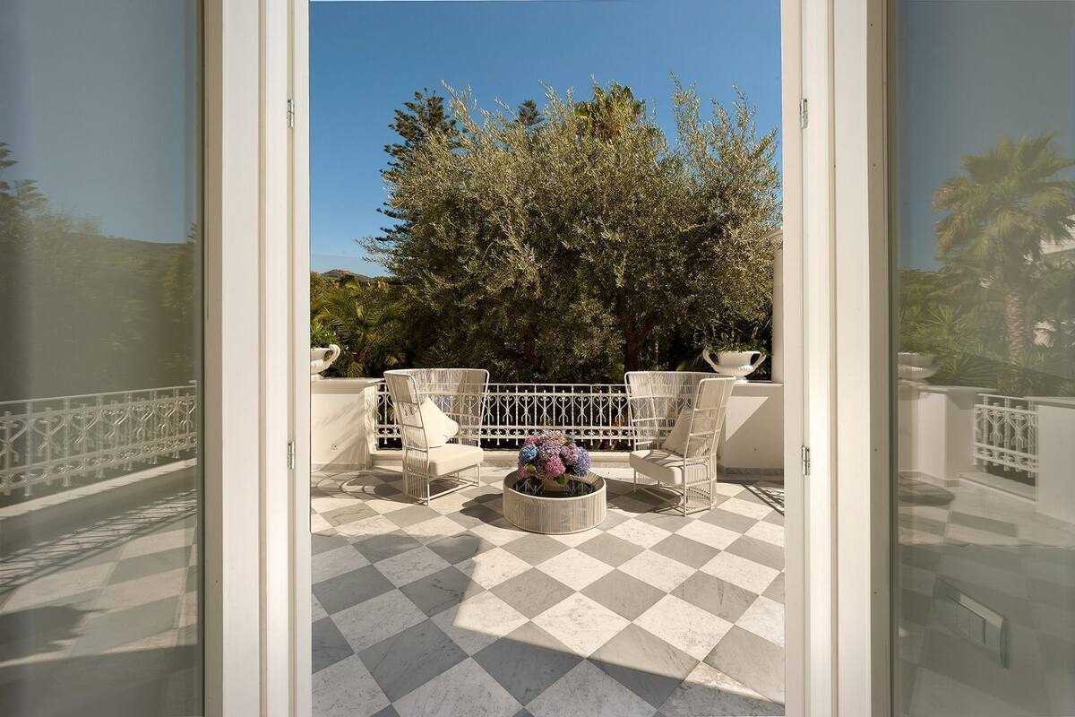 A balcony with checkered flooring, white wicker furniture, and a potted plant.