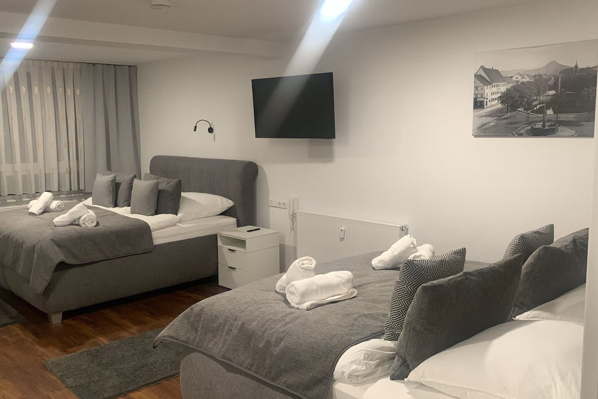 Une chambre d’hôtel avec deux lits, un téléviseur à écran plat, une fenêtre avec des rideaux et un tableau encadré au mur.