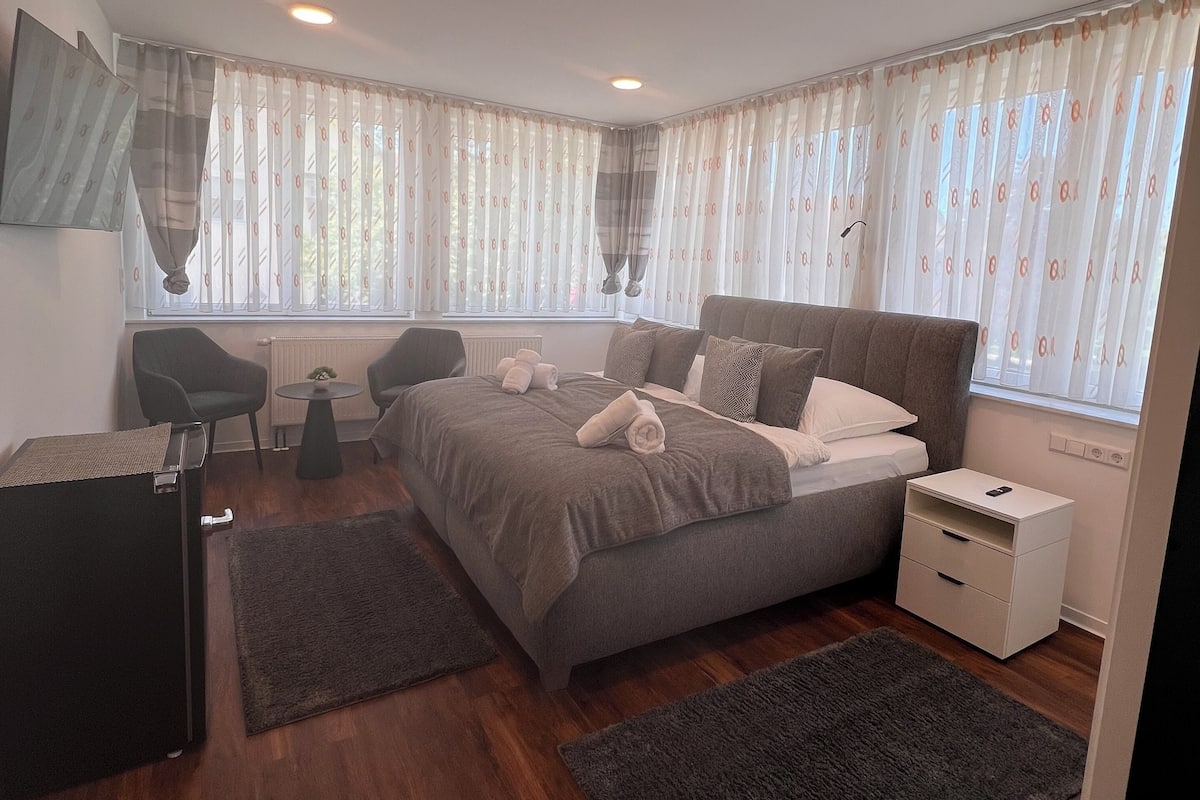 Une chambre à coucher comprenant un lit, des tables de chevet, une chaise, une petite table et un radiateur.