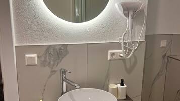 Un bagno con uno specchio rotondo, un lavandino bianco e un asciugacapelli montato a parete.