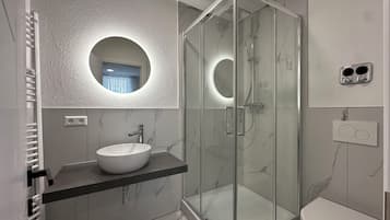 A modern bathroom with a glass-enclosed shower, a white sink, and a toilet.