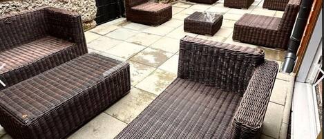 Een terras met rieten meubels, waaronder banken en stoelen, op een betegelde vloer.